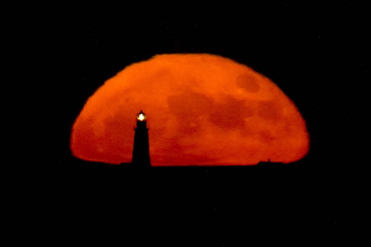 A full moon rises behind the Boston Light, late Tuesday, June 14, 2022, in Winthrop, Mass. The ...