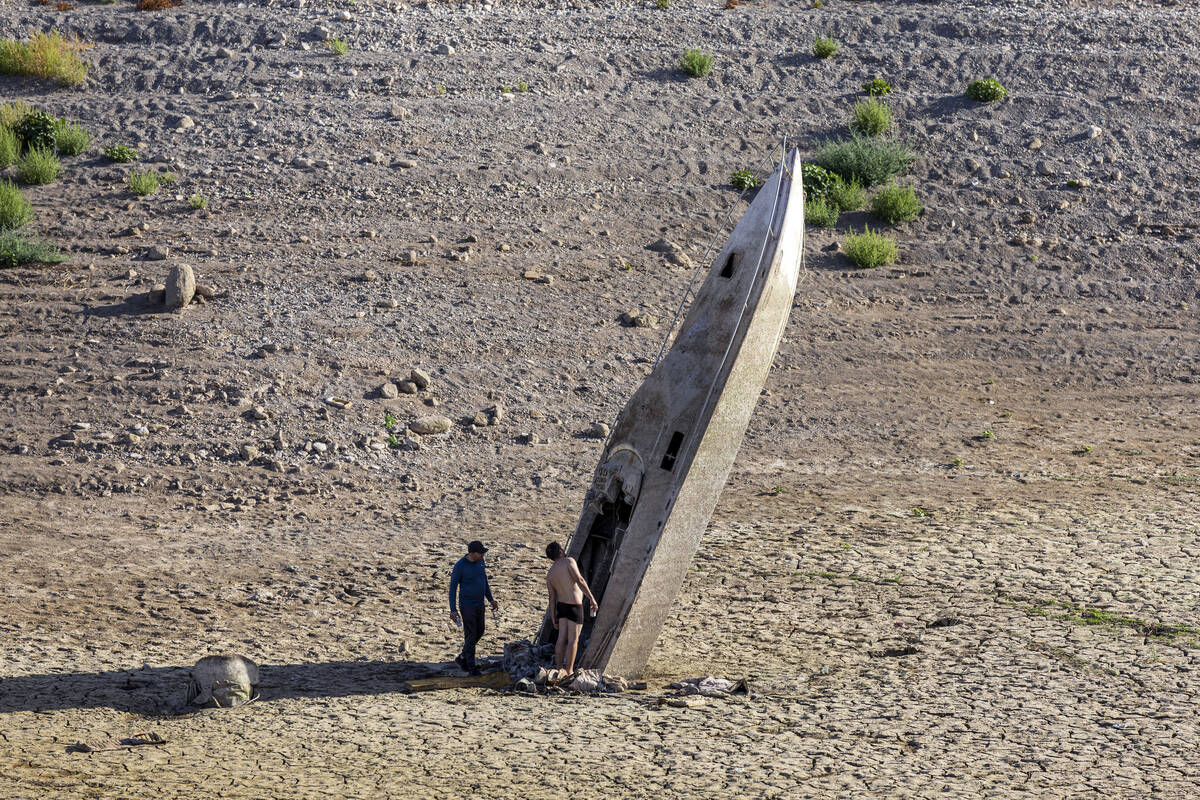 Two men check out a boat stuck straight up along the shoreline as water levels continue to drop ...