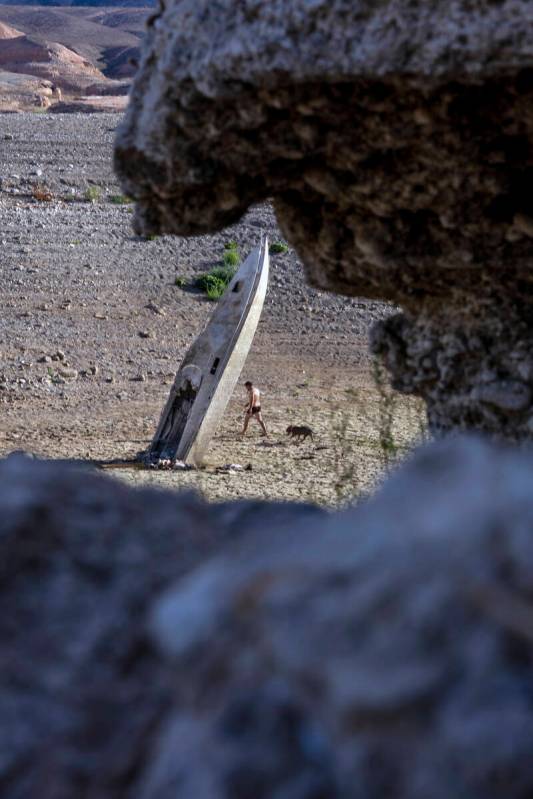 A man and dog walk past a boat stuck straight up along the shoreline as water levels continue t ...