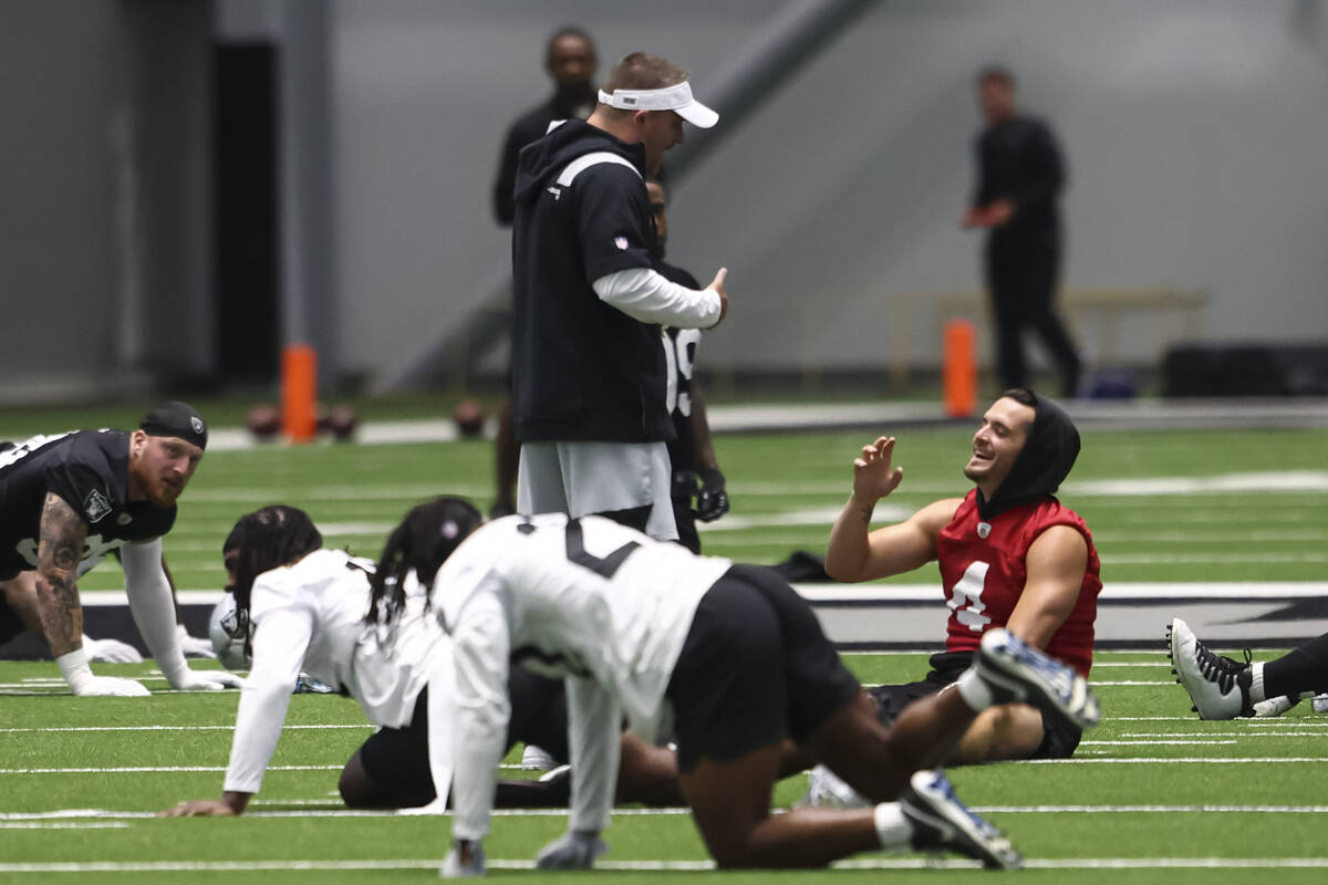 Raiders head coach Josh McDaniels talks with quarterback Derek Carr as players stretch during m ...