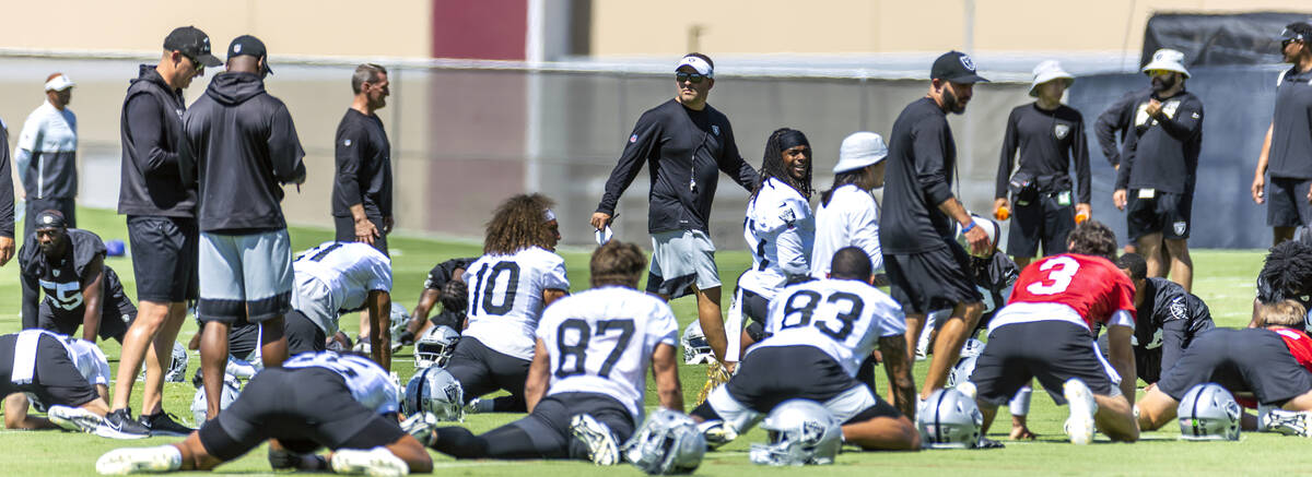 Raiders head coach Josh McDaniels walks past stretching players during minicamp practice at the ...