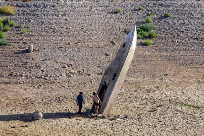 Dua pria melihat sebuah perahu yang terjebak tegak di sepanjang garis pantai saat permukaan air terus menurun…