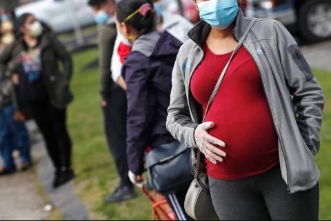 FILE - In this May 7, 2020 file photo, a pregnant woman wearing a face mask and gloves holds he ...