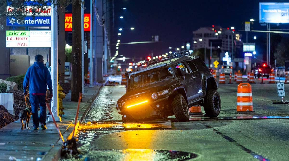 Seorang pejalan kaki melihat kendaraan yang terjebak dalam lubang konstruksi akibat banjir di dekat Charleston...