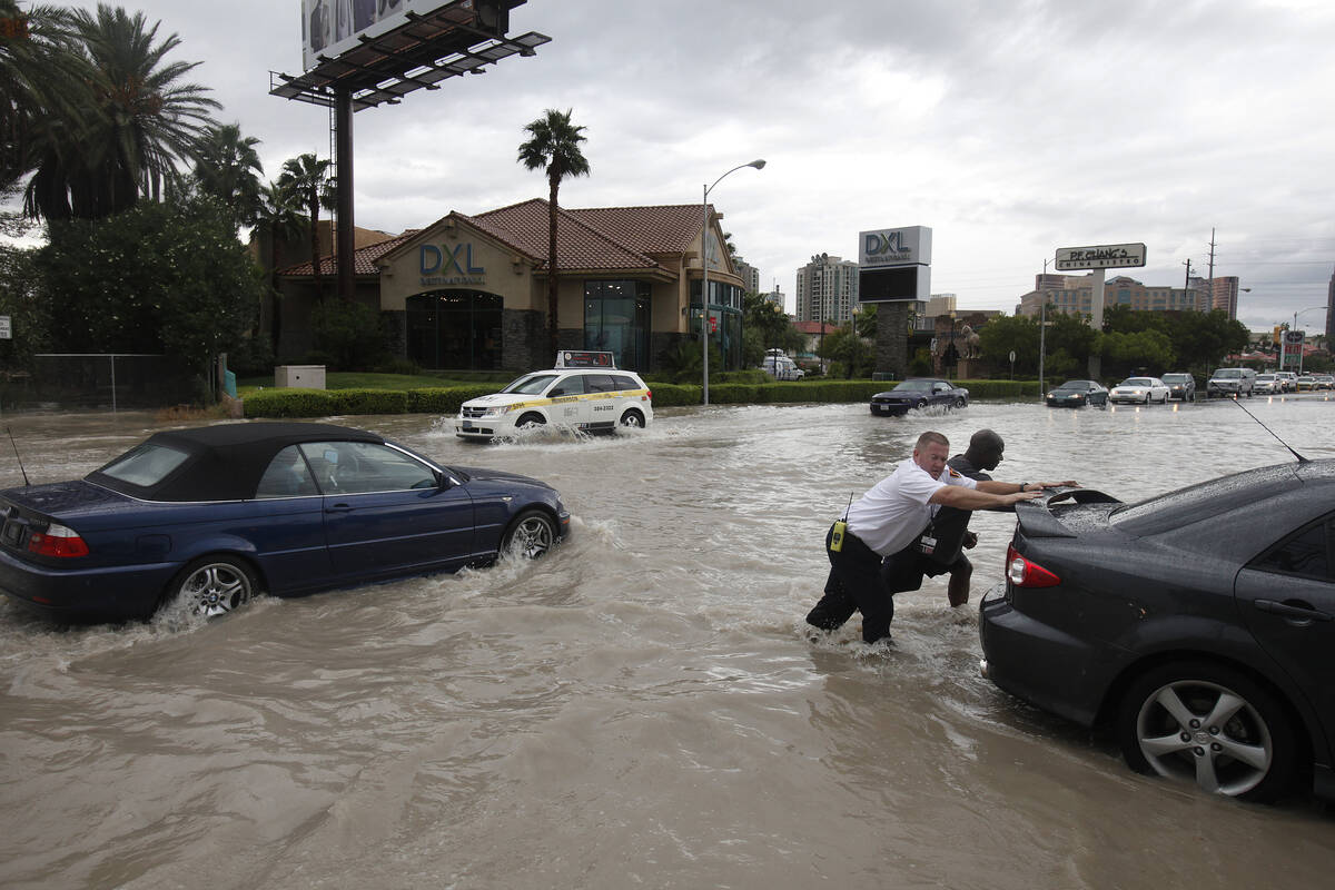 People push a stalled car off a flooded street in Las Vegas on Sept. 11, 2012. (AP Photo/Las Ve ...
