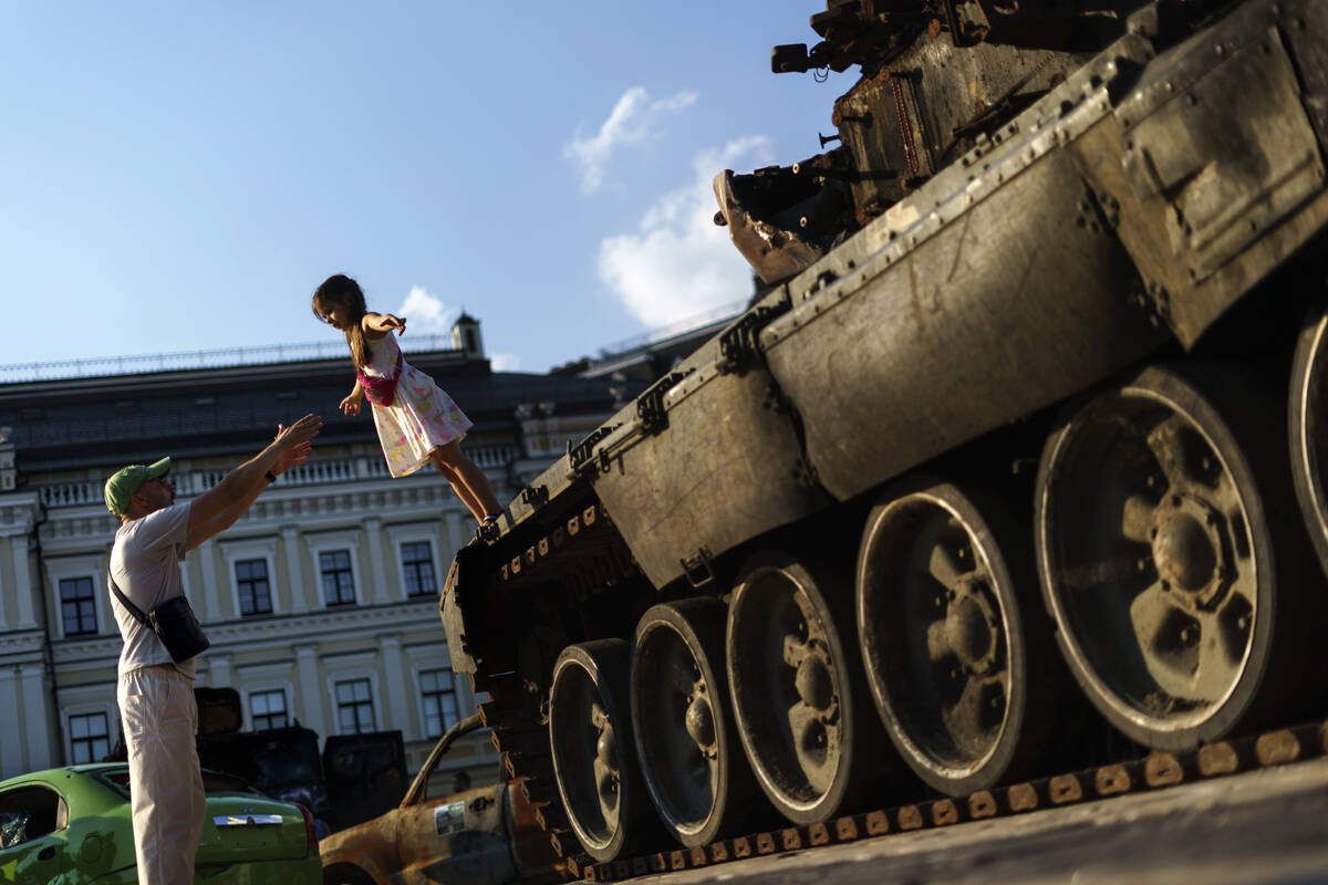 A young girl falls into her father's arms off a Russian tank that was destroyed and exhibited a ...