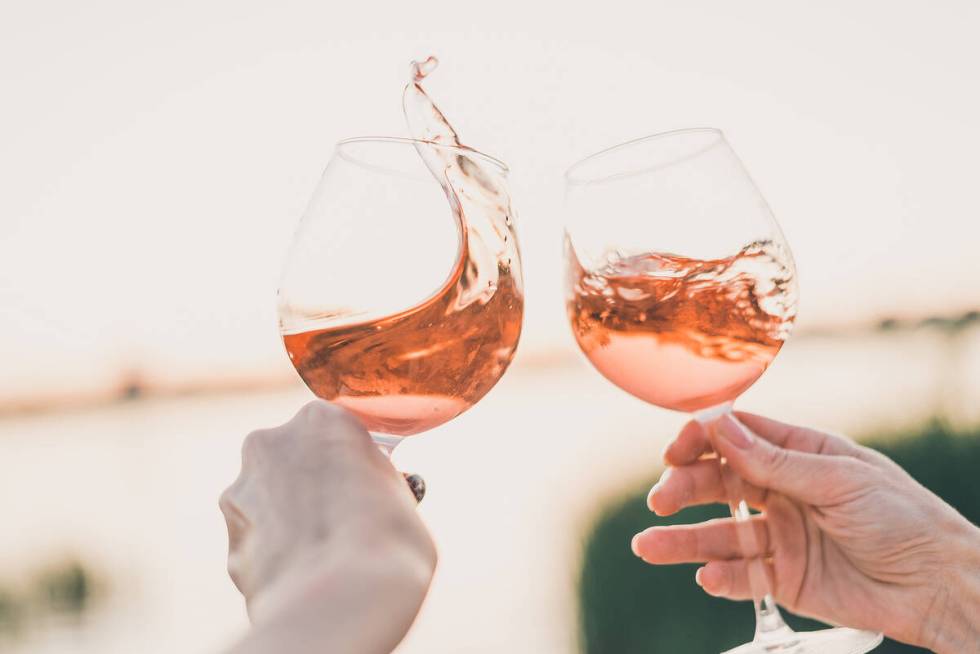 Two glasses of rose wine in hands against the sunset sky. Cropped.