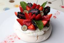 Pavlova, a crunchy meringue with a soft center, topped with fresh berries, berry dust, and mint ...