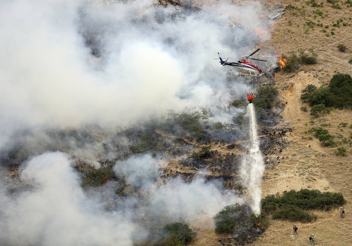 Firefighters battle a wildfire from the ground as a helicopter drops water above them in Spring ...