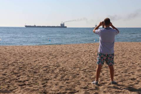 A man takes a picture as the Glory bulk carrier makes its way from the port in Odesa, Ukraine, ...