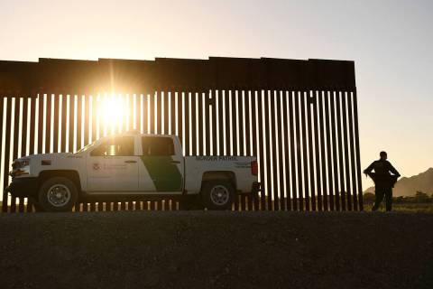 A Border Patrol agent walks between a gap along the border wall between the U.S. and Mexico in ...