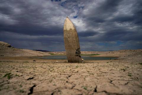 A formerly sunken boat stands upright into the air with its stern buried in the mud along the s ...