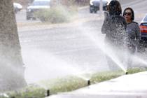 Pedestrians wait to cross Green Valley Parkway as lawn sprinklers water grass in March 2019 in ...