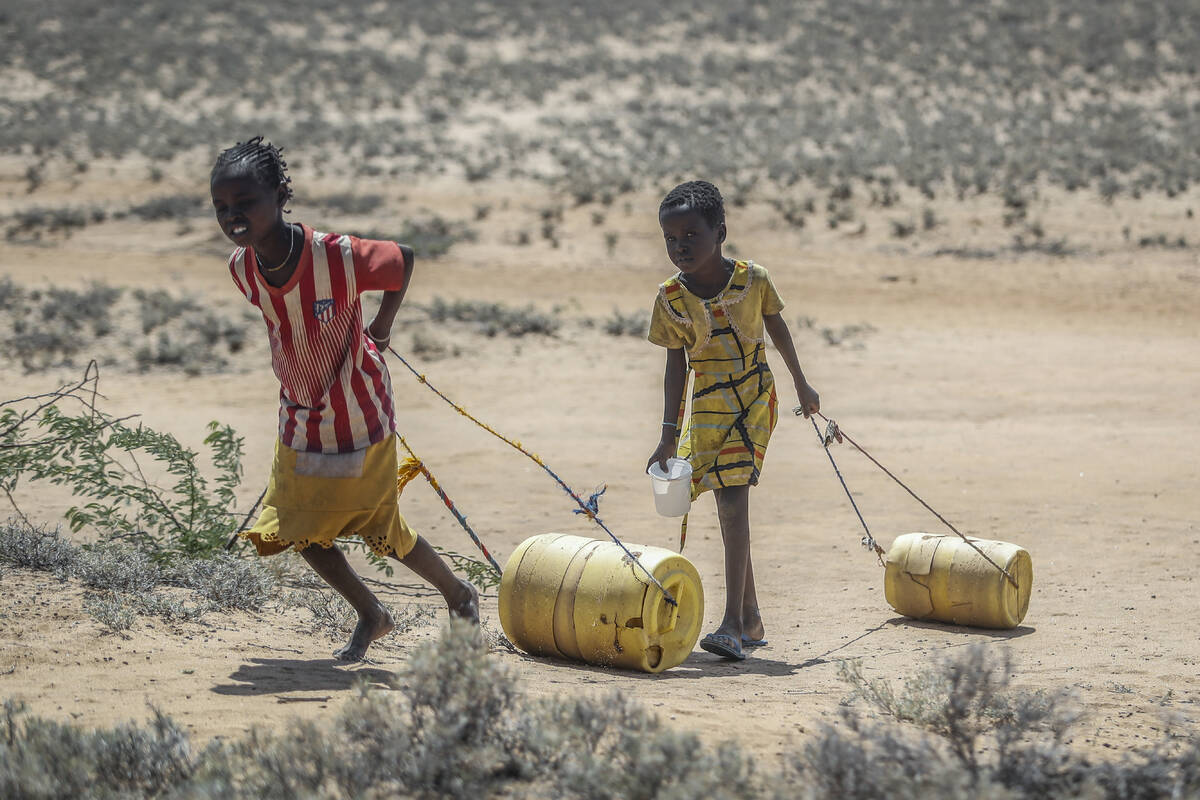 FILE - Young girls pull containers of water as they return to their huts from a well in the vil ...
