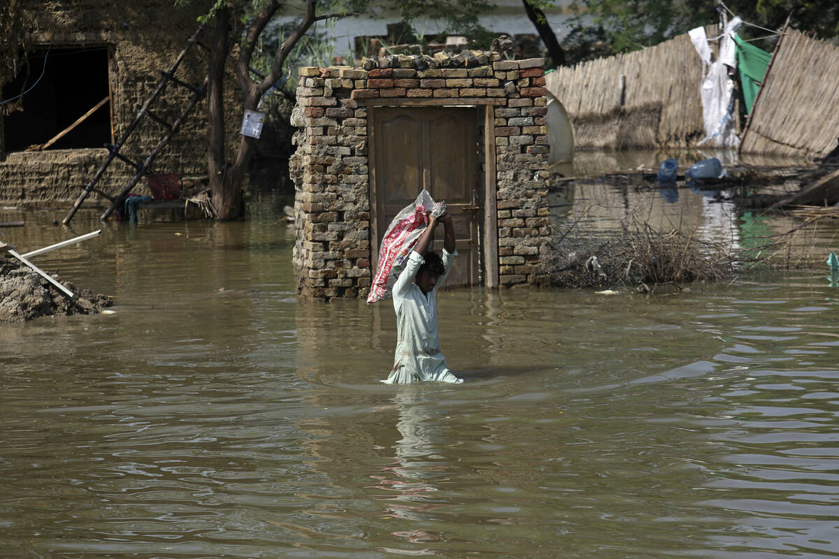 FILE - A man carries usable belongings salvaged from his flood-hit home across a flooded area i ...