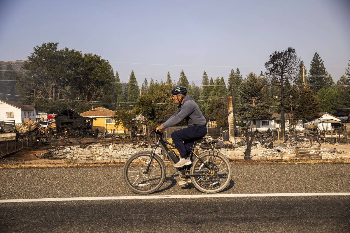 A cyclist rides along homes destroyed by the Mill Fire along U.S. 97 in Weed, Calif., Saturday, ...