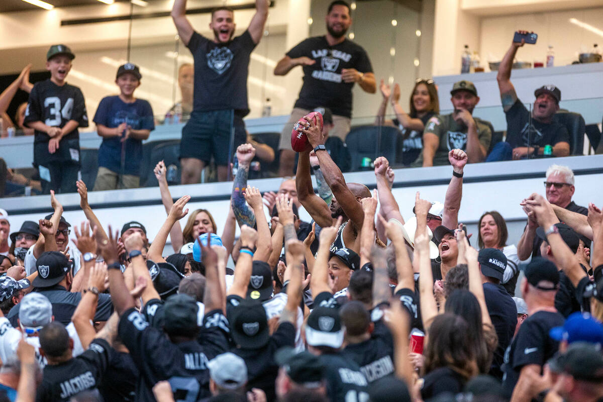 A Raiders fan holds up a football in the stands as others cheer during the first half of their ...