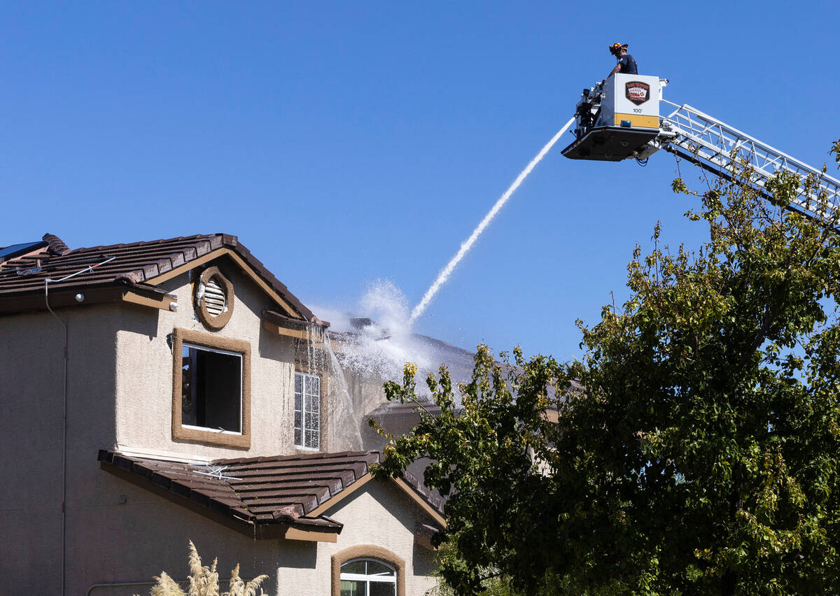 A Las Vegas firefighter sprays water on a two-story home where two people were found dead after ...
