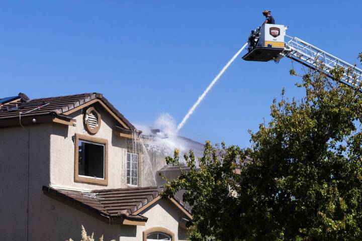 A Las Vegas firefighter sprays water on a two-story home where two people were found dead after ...