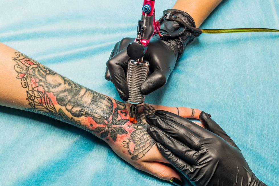 Artis tato close-up mendemonstrasikan proses mendapatkan tato hitam dan merah dengan pai jingga...