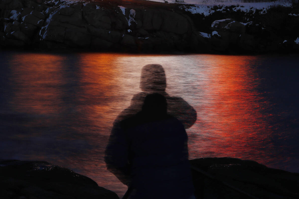 FILE - In this photo made with a long exposure, a man is silhouetted against lights reflected i ...