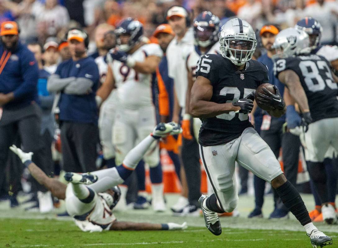 Raiders running back Zamir White (35) trips up Denver Broncos safety Kareem Jackson (22) as he ...
