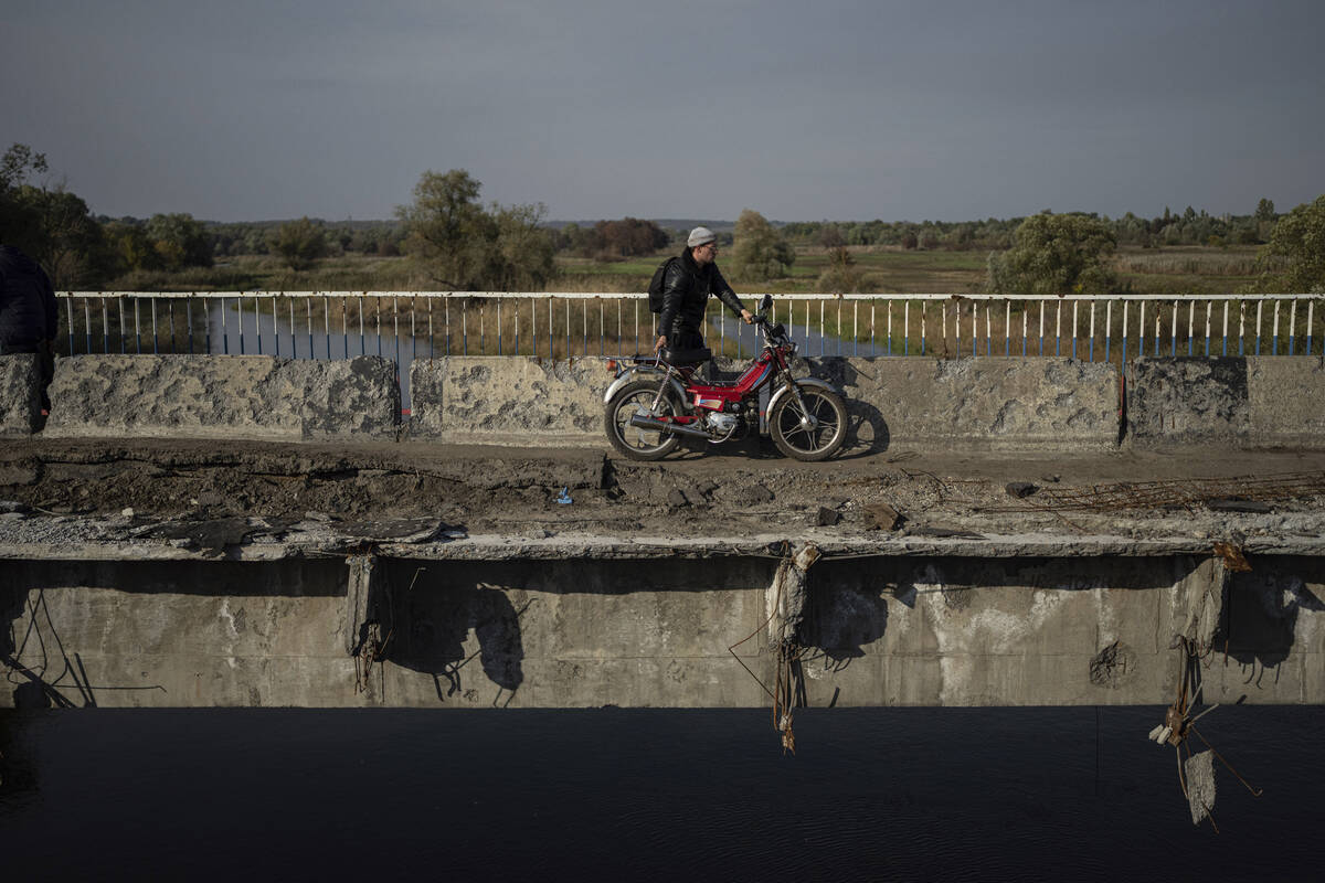 A man hauls his motorbike on a destroyed bridge across Oskil river during evacuation in recentl ...
