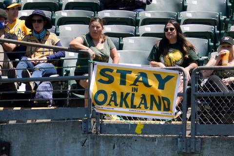 Fans sit behind a sign that reads "Stay in Oakland" during the first inning of a baseball game ...