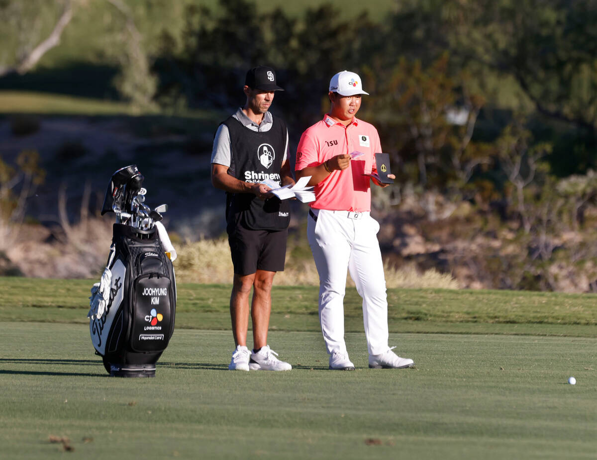 Tom Kim discusses with his caddie as he prepares to drive to the eighteenth green during the th ...