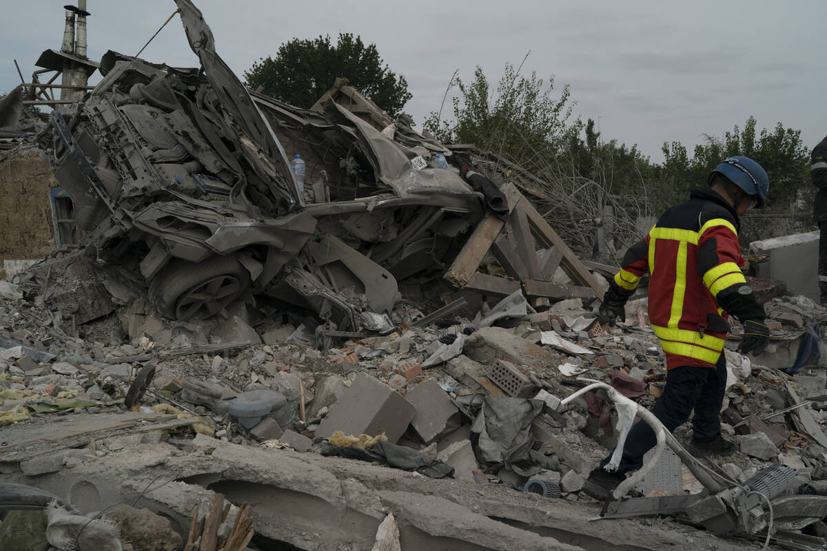 A rescue worker walks past a wrecked car on a site where several houses were destroyed after a ...