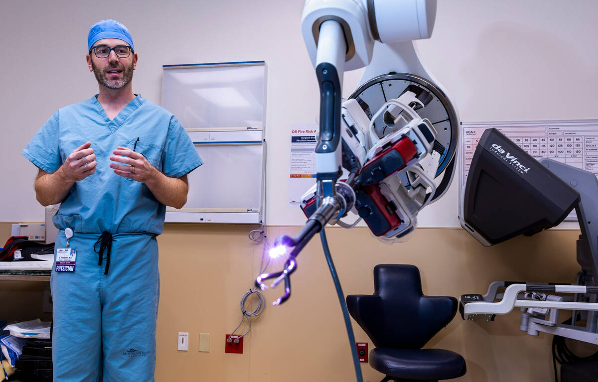 Dr. Garrett Friedman stands by a da Vinci SP surgical robot with patient cart, center, and cons ...