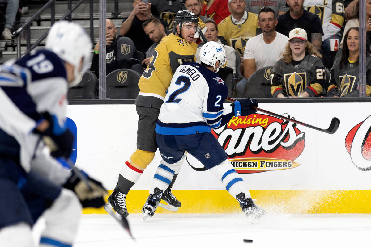 Jets defenseman Dylan DeMelo (2) slams Golden Knights right wing Reilly Smith (19) into the boa ...