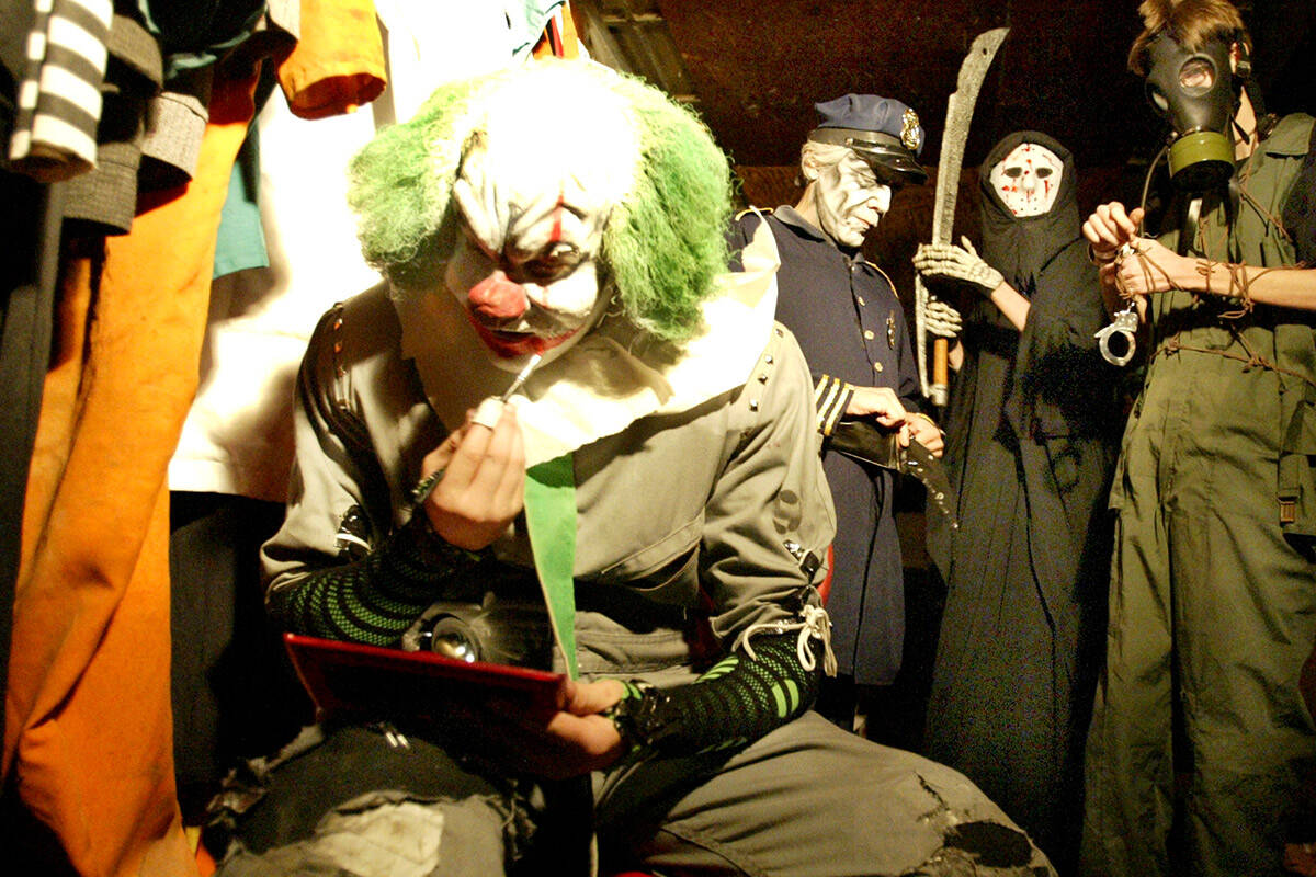 A scary clown puts red paint on his mouth as cast members gear up to work in the Fright Dome at ...