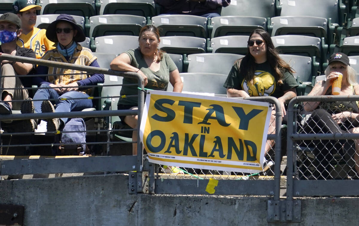 Fans sit behind a sign that reads "Stay in Oakland" during the first inning of a baseball game ...