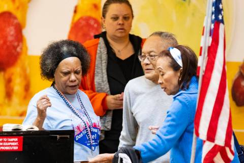 Alicia John, an election worker, watches as voters, who declined to give their names, place the ...