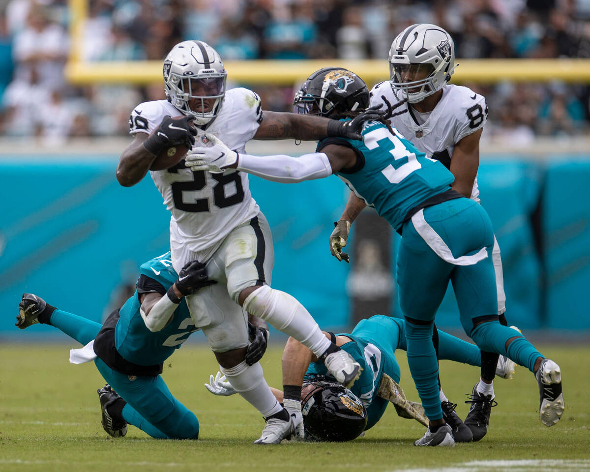 Raiders running back Josh Jacobs (28) is wrapped by Jacksonville Jaguars cornerback Darious Wil ...