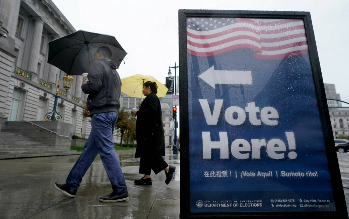 People carry umbrellas while walking past a voting sign outside City Hall in San Francisco, Tue ...