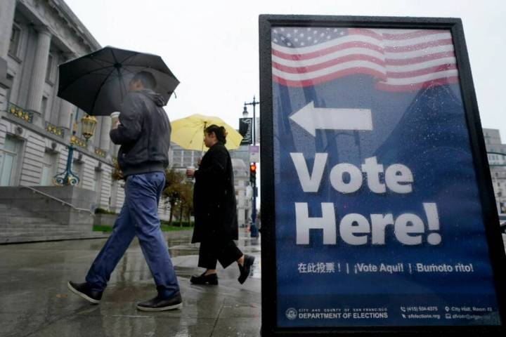 People carry umbrellas while walking past a voting sign outside City Hall in San Francisco, Tue ...