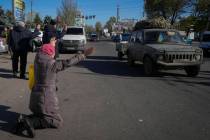 A woman kneels on the ground in front of passing Ukrainian Army car in Kherson, Ukraine, Tuesda ...