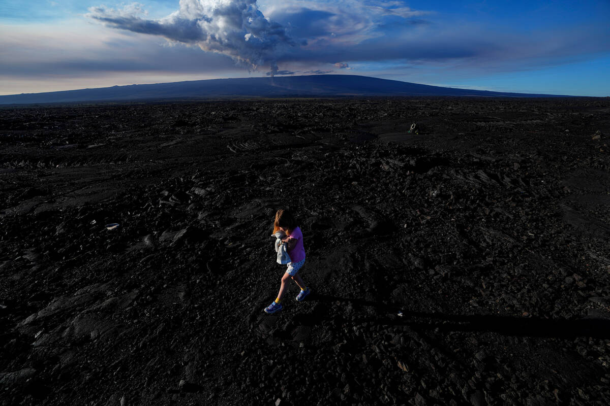 Abigail Dewar, of Alberta, Canada, holds a stuffed animal as she walks over hardened lava rock ...