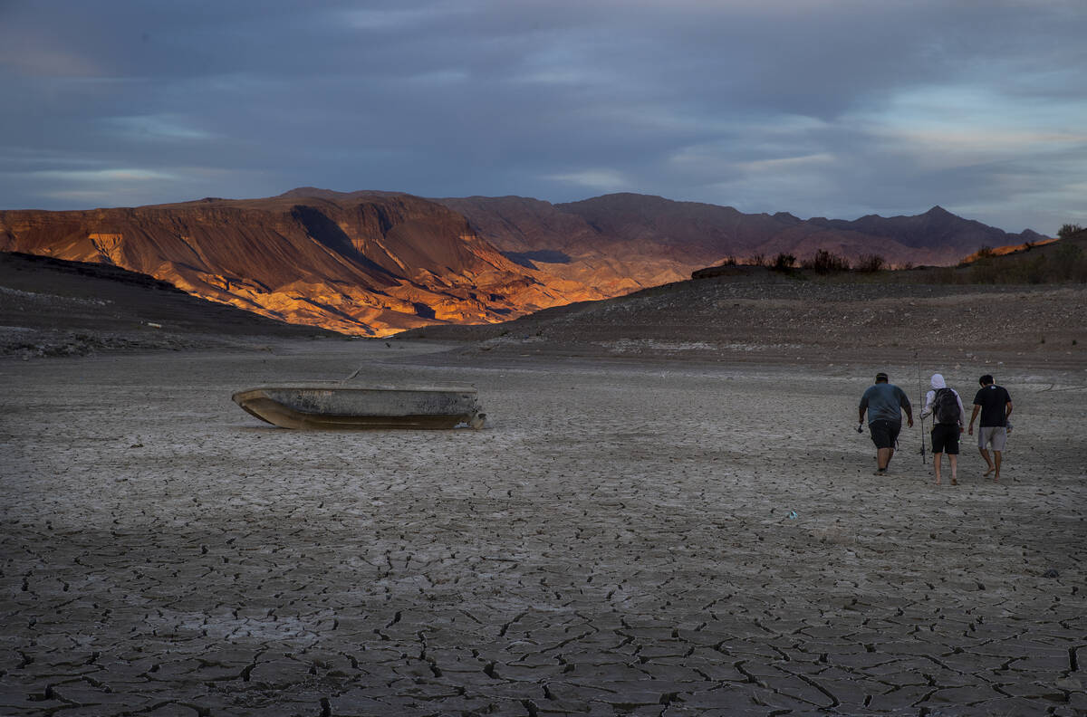 Fishermen walk past an old boat left behind as the waterline continues to recede about the clos ...