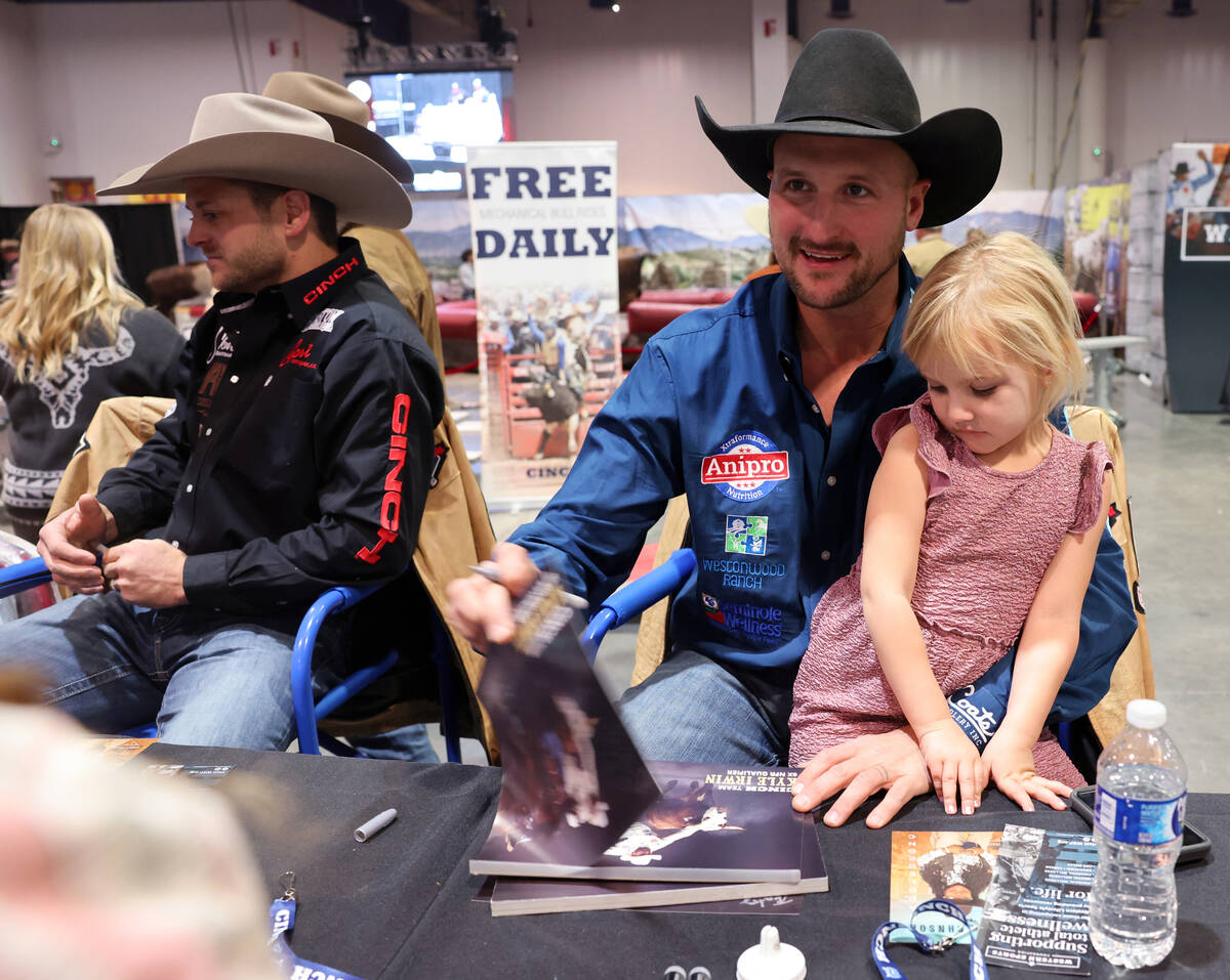 NFR steer wrestler Kyle Irwin signs autographs with his daughter Ellie Irwin, 4, at the Cinch b ...