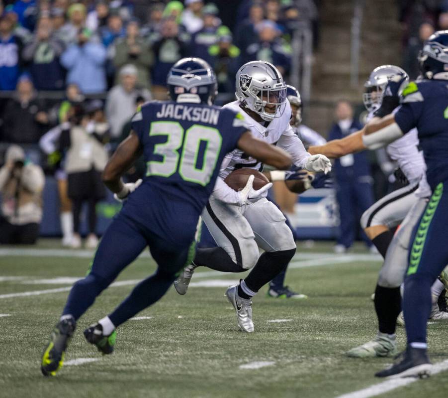 Raiders running back Josh Jacobs (28) looks for room as Seattle Seahawks cornerback Mike Jackso ...