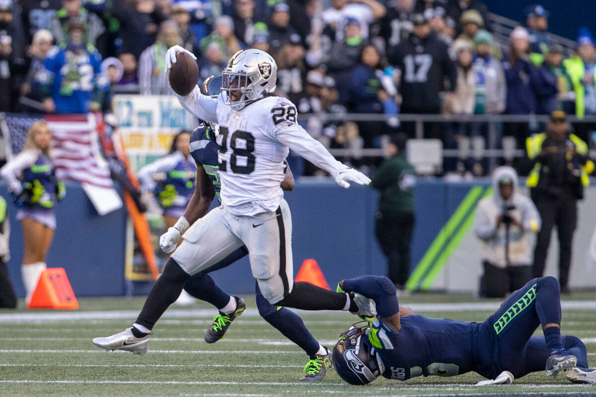 Raiders running back Josh Jacobs (28) looks to escape a tackle by Seattle Seahawks safety Quand ...