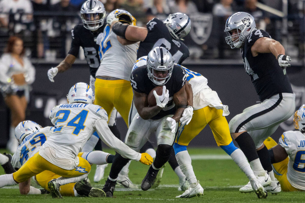 Raiders running back Josh Jacobs (28) pushes Los Angeles Chargers defenders through for more ya ...