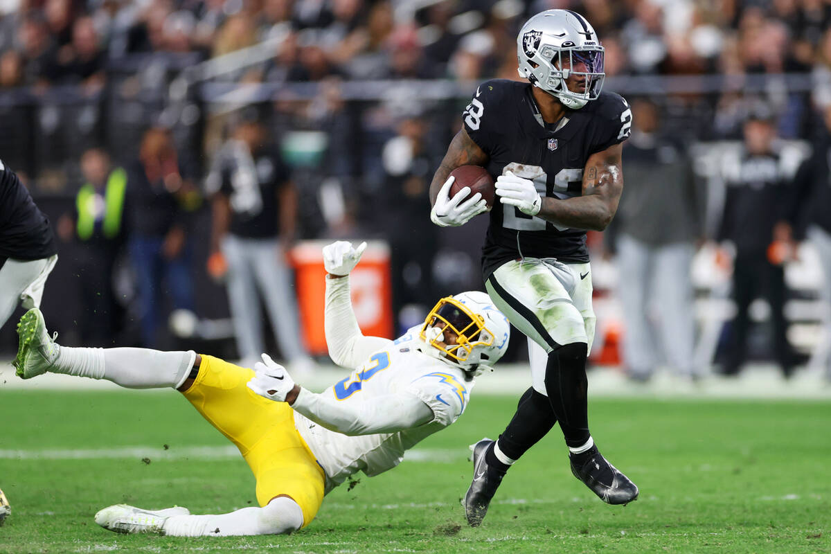 Raiders running back Josh Jacobs (28) runs the ball after avoiding a table from Los Angeles Cha ...