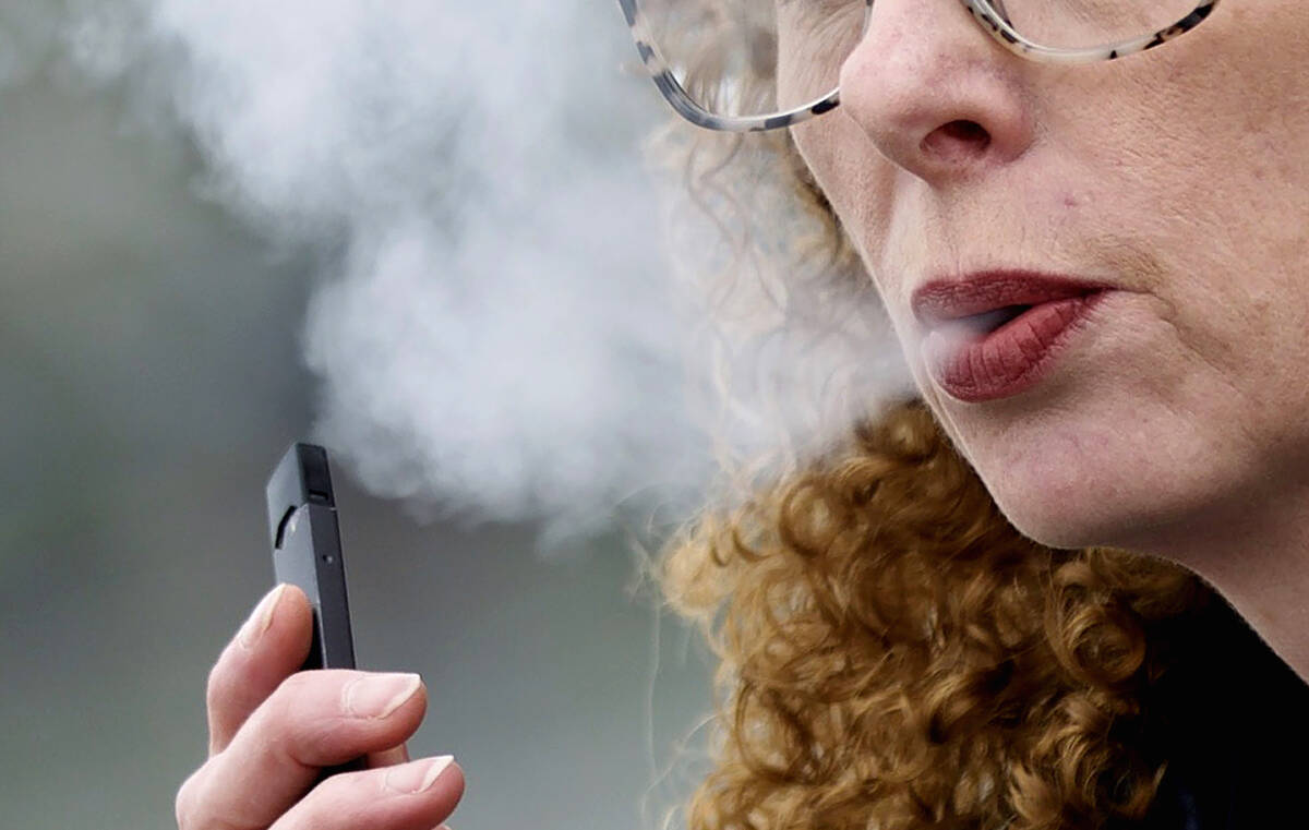 A woman exhales while vaping from a Juul pen e-cigarette in Vancouver, Wash., April 16, 2019. ( ...
