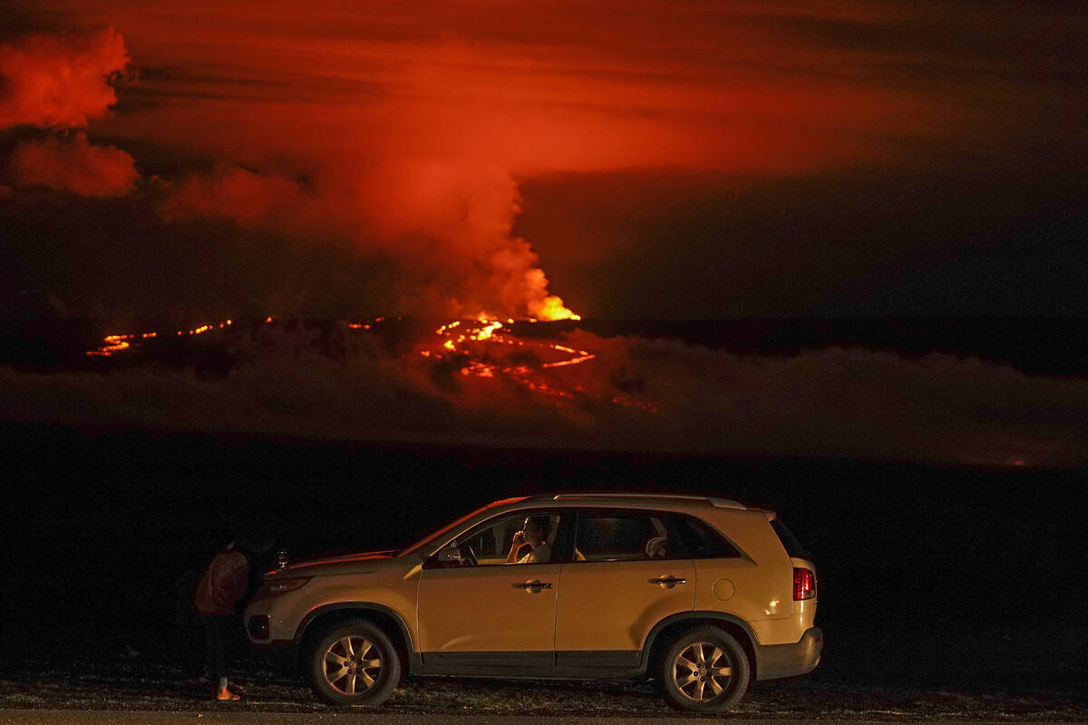 FILE - A man talks on a phone in his car alongside Saddle Road as the Mauna Loa volcano erupts ...