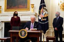 President Joe Biden signs executive orders after speaking about the coronavirus, accompanied by ...
