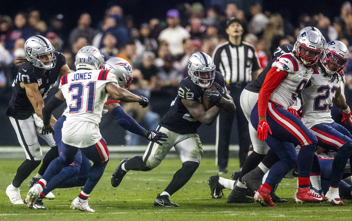 Raiders running back Josh Jacobs (28) breaks through the line as New England Patriots cornerbac ...